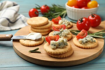 Tasty crackers with blue cheese, rosemary and tomatoes on wooden table, closeup
