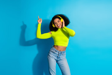 Young cheerful woman enjoying music in neon outfit posing happily against a bright blue background...