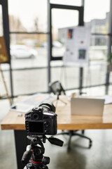 A well organized workspace displays a camera on a tripod next to a laptop and project materials