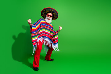 Cheerful elderly man in vibrant traditional Mexican attire celebrates against a green background