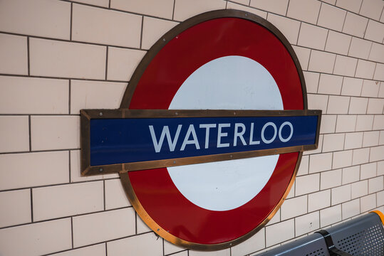Fototapeta The iconic red and blue roundel sign for Waterloo station is mounted on a tiled wall. A metallic and orange bench is partially visible in the corner.