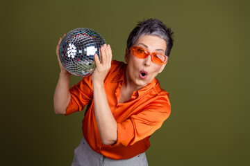 Confident elegant woman with a disco ball showcasing style and charm in an orange outfit against a...