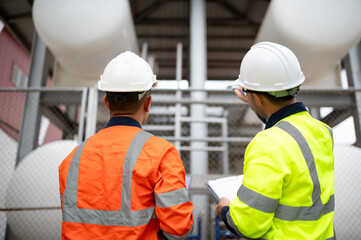 Two maintenance engineers are inspecting a large gas tank
