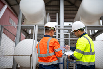 Two maintenance engineers are inspecting a large gas tank