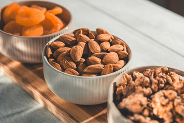 Three bowls of healthy snacks including dried apricots, walnuts, and almonds are arranged on a...
