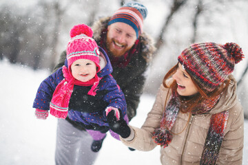 Fototapeta premium Young family with baby girl having fun in the snow