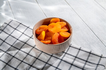 Brimming with dried apricots. A beige bowl rests on a checkered cloth. Creating a vibrant display of color and texture that highlights the natural sweetness and nutritious appeal of this healthy snack