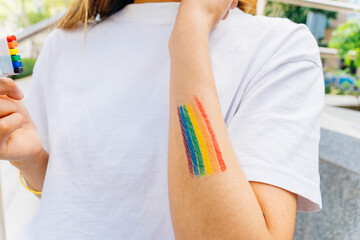 Rainbow-painted woman wearing white t-shirt displaying lgbt pride flag on arm, supporting diversity...