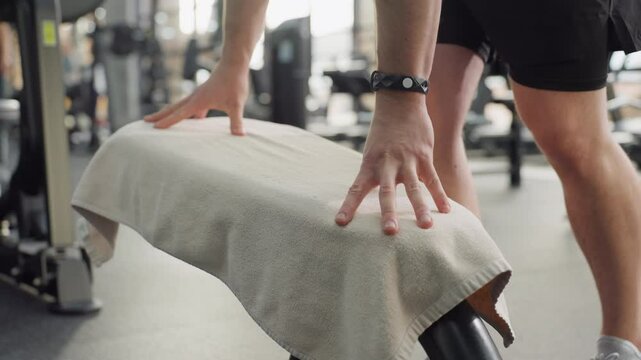 Close up of weight bench as gym goer places towel on seat pad before workout showing clean routine and equipment prep in well lit modern fitness space ensuring hygienic environment