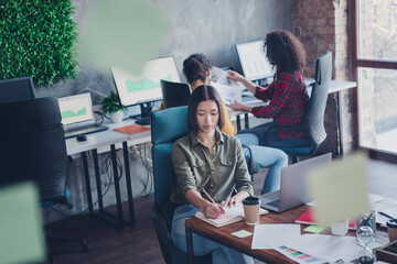 Young focused professionals collaborating in a modern coworking space with green decor, working on project