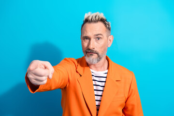 Naklejka premium Confident mature man in orange jacket pointing with gesture, charismatic and stylish against blue background, embodies elegance
