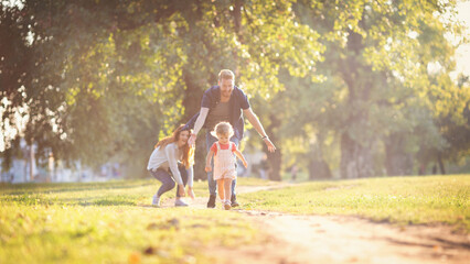 Fototapeta premium Young happy parents with their baby girl having fun outdoors