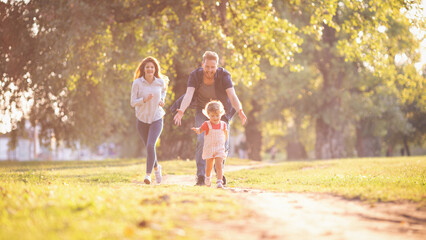 Fototapeta premium Young happy parents with their baby girl having fun outdoors