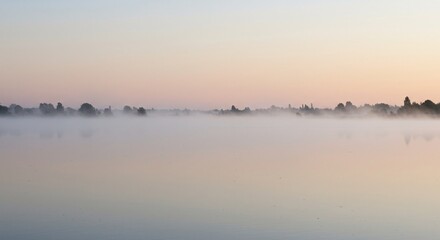 Naklejka premium Misty Sunrise over Serene Lake A Breathtaking Panorama of Nature's Tranquility
