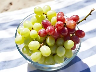 Fresh green and red grapes displayed in a glass bowl on a striped beach towel.