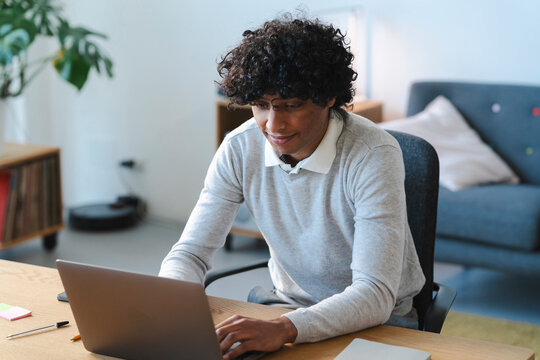 An Arab young man works on his laptop at home. He is focused on his work and seems to be enjoying the task at hand.