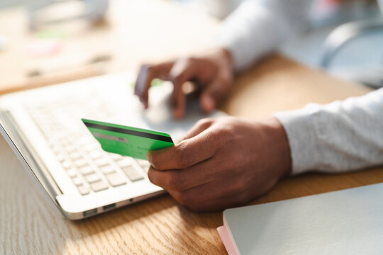 A young Arab man is shopping online. He is holding a credit card in one hand and typing on a laptop with the other.