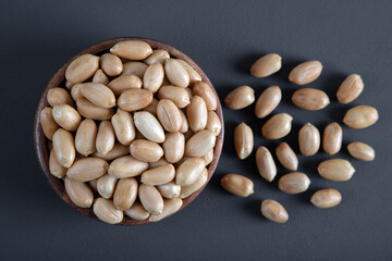 Bowl full of roasted peeled peanuts on dark background,top view