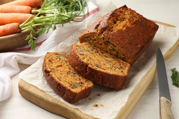 Homemade carrot cake with nuts, vegetables and knife on white wooden table, closeup