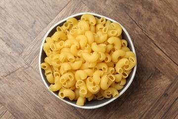 Raw horns pasta in bowl on wooden table, top view