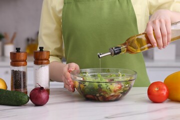 Woman pouring oil onto tasty salad at white marble table in kitchen, closeup