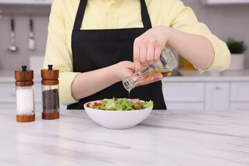 Woman pouring oil onto tasty salad at white marble table in kitchen, closeup