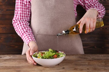 Woman pouring oil onto tasty salad at wooden table, closeup
