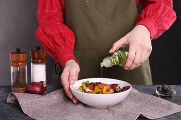 Woman pouring oil onto tasty salad at dark textured table, closeup