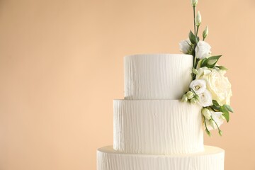 Delicious wedding cake decorated with flowers on beige background, closeup. Space for text