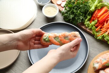 Woman making tasty spring roll at grey wooden table, closeup