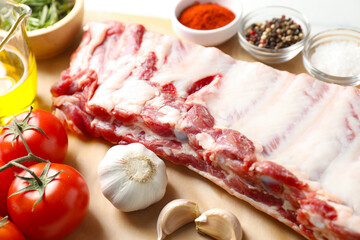 Raw pork ribs, spices and tomatoes on white table, closeup