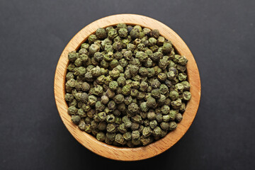 Aromatic pepper in bowl on dark table, top view