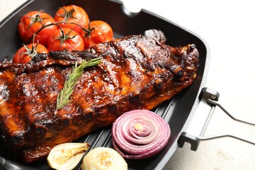 Delicious roasted pork ribs with rosemary, tomatoes and onions on light table, closeup