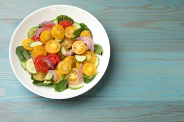 Fresh salad with yellow tomatoes on light blue wooden table, top view. Space for text