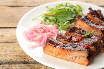 Delicious pork ribs, arugula and onion on wooden table, closeup