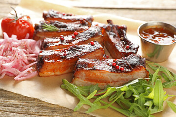 Delicious pork ribs, sauce, arugula and onion on wooden table, closeup