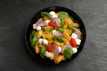 Tasty salad with yellow tomatoes, basil, onion and mozzarella cheese on black table, top view