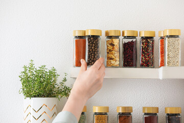 Woman taking glass jar of allspice from shelf indoors, closeup