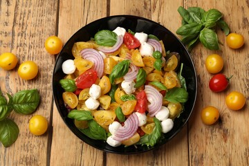 Tasty salad with yellow tomatoes, basil, onion and mozzarella cheese on wooden table, flat lay