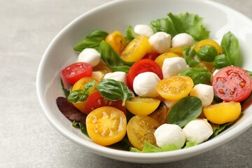 Tasty salad with yellow tomatoes, basil and mozzarella cheese on light grey table, closeup