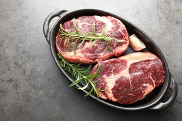 Pieces of raw beef meat and spices in baking dish on gray textured table, top view