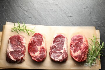 Pieces of raw beef meat, rosemary and salt on black table, top view. Space for text