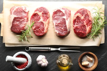Pieces of raw beef meat, spices and carving fork on black table, flat lay