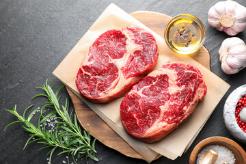 Pieces of raw beef meat and spices on black table, flat lay