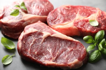 Pieces of raw beef meat and basil on grey table, closeup