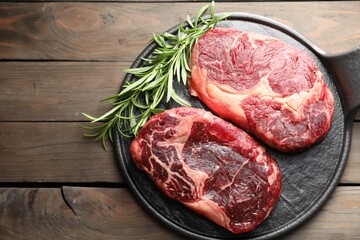 Pieces of raw beef meat and rosemary on wooden table, top view. Space for text