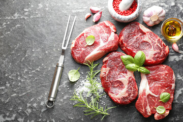 Pieces of raw beef meat, spices and carving fork on dark table, flat lay. Space for text