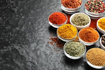 Different aromatic spices in bowls on dark table, above view. Space for text