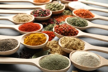 Many different spices in spoons on grey table, closeup