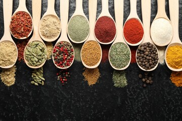 Many different spices in spoons on black table, flat lay